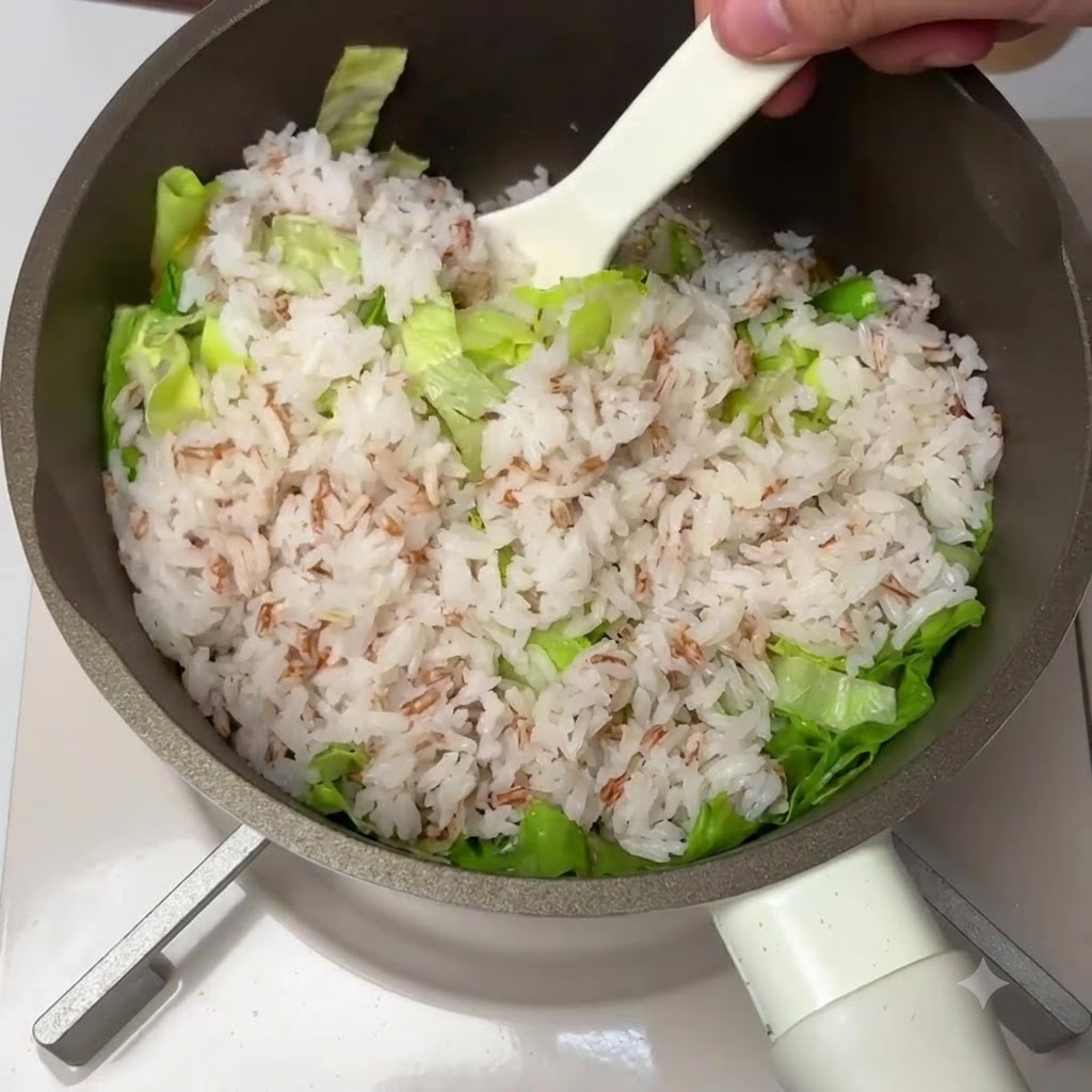 フライパンの中で、白ヘラを使ってご飯、新鮮なレタス、トマトミックスをしっかりと混ぜ合わせている様子。
