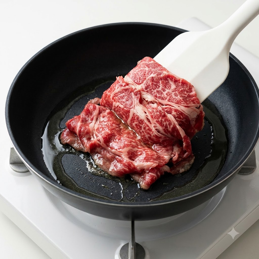 熱したフライパンの油の中に、白いヘラを使って生のマリネ牛肉を入れている様子。