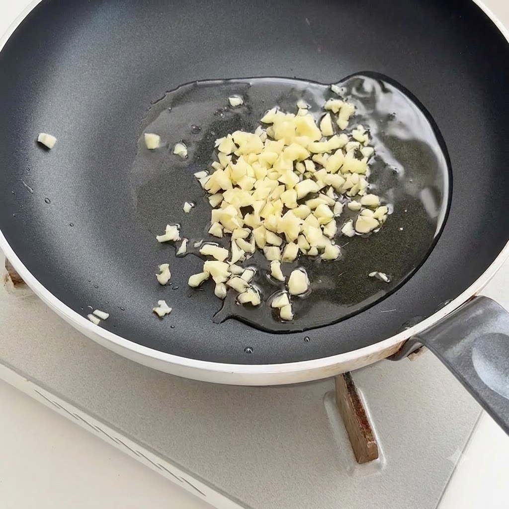 焦げ付きにくいフライパンの中央で、熱い油の中でみじん切りにんにくが音を立てて炒められている様子。