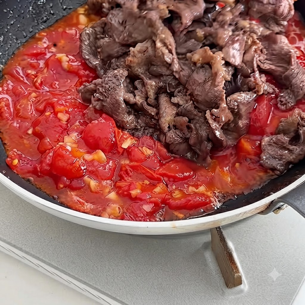 とろみのある赤いトマトソースの入ったフライパンに、火を通した牛肉を戻し入れている様子。