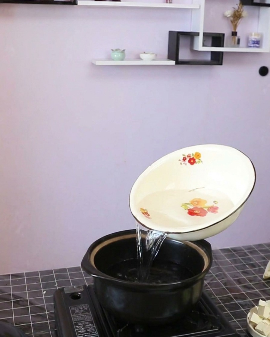 清澈的水从精美的白碗中倒入深色砂锅内。
