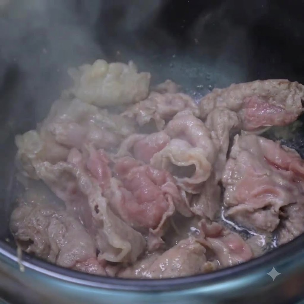 調理鍋の中で、炒めた牛肉と一緒にスプーン一杯のすりおろしニンニクと刻みネギを炒め合わせている様子。