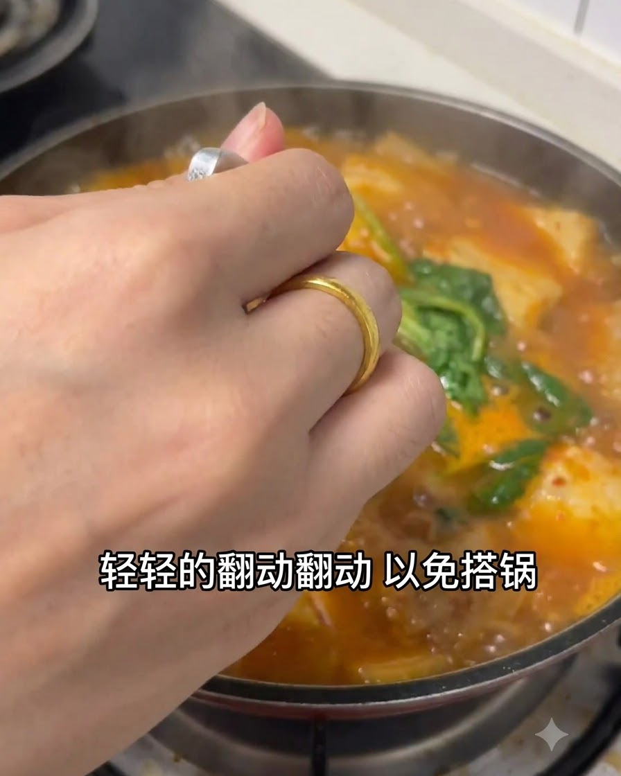 スプーンを使って、鍋の中でグツグツと煮えるオレンジ色のチゲを優しくかき混ぜる手。