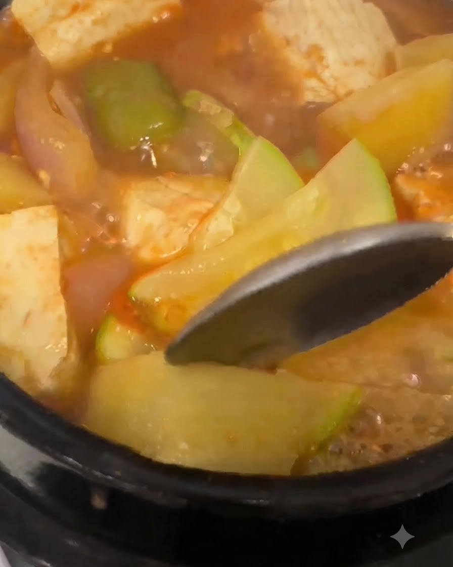 韓国味噌チゲの中で、柔らかくなったじゃがいものスライスにスプーンを押し当てている様子。