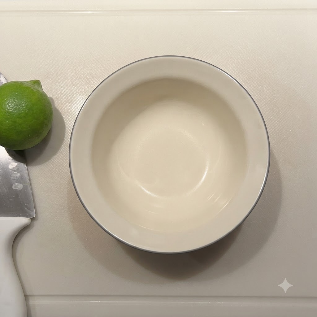 まな板の上に置かれたフレッシュなライムとナイフの隣に、空の小さな陶器製ボウルがある様子。