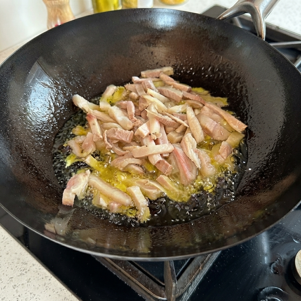 黒い中華鍋の中で熱い油に包まれながらジュージューと揚げられている豚肉の細切り。