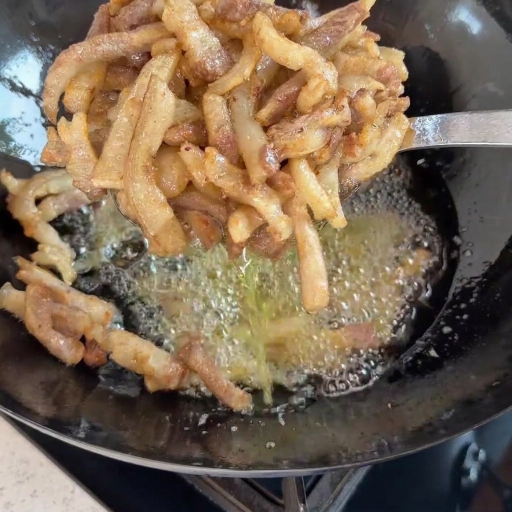 泡立つ油の中華鍋の上で、揚げたてのきつね色の豚肉をすくい網で持ち上げている様子。