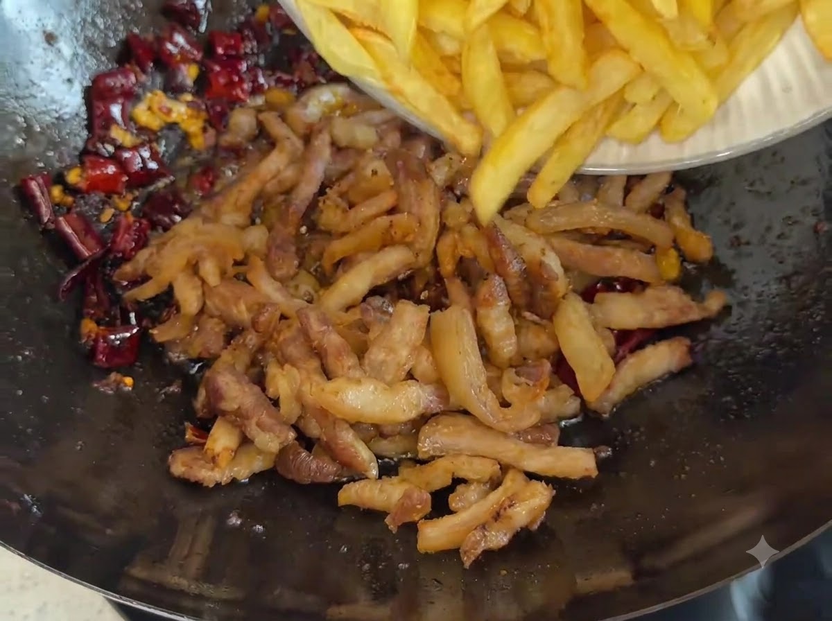 揚げた豚肉と濃い赤色のチリスパイスが入った中華鍋へ、フライドポテト状の黄金色のジャガイモが皿から滑り落ちているところ。