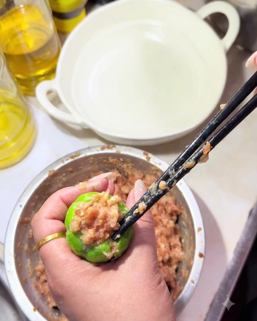 片手で種をくり抜いたピーマンを持ち、箸で肉種を中に押し込んでいる様子