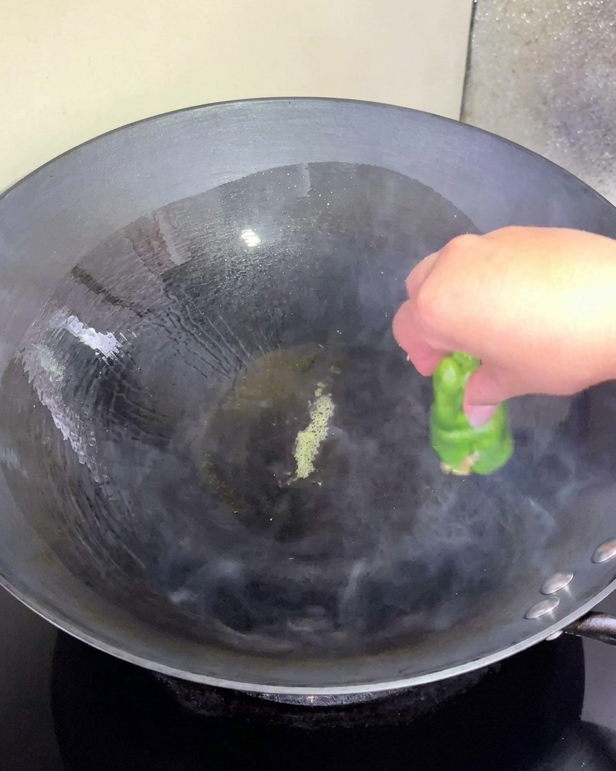 油をひいた熱いフライパンに肉詰めのピーマンをそっと置いている手
