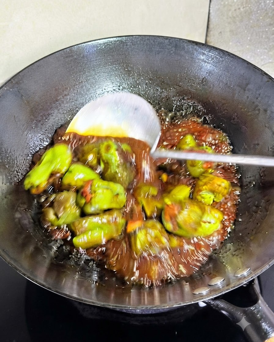 フライパンの中で、とろみのある黒いタレと一緒に混ぜられているピーマンの肉詰め