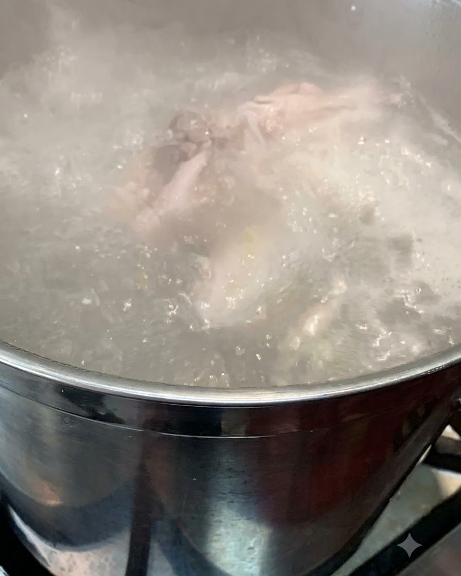 下茹でされた骨と一緒に、沸騰した鍋の中に丸鶏が沈められている様子。