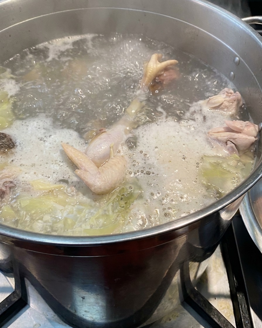 沸騰しているスープと材料が入った大きな寸胴鍋に、豚背脂の塊が投入されているところ。