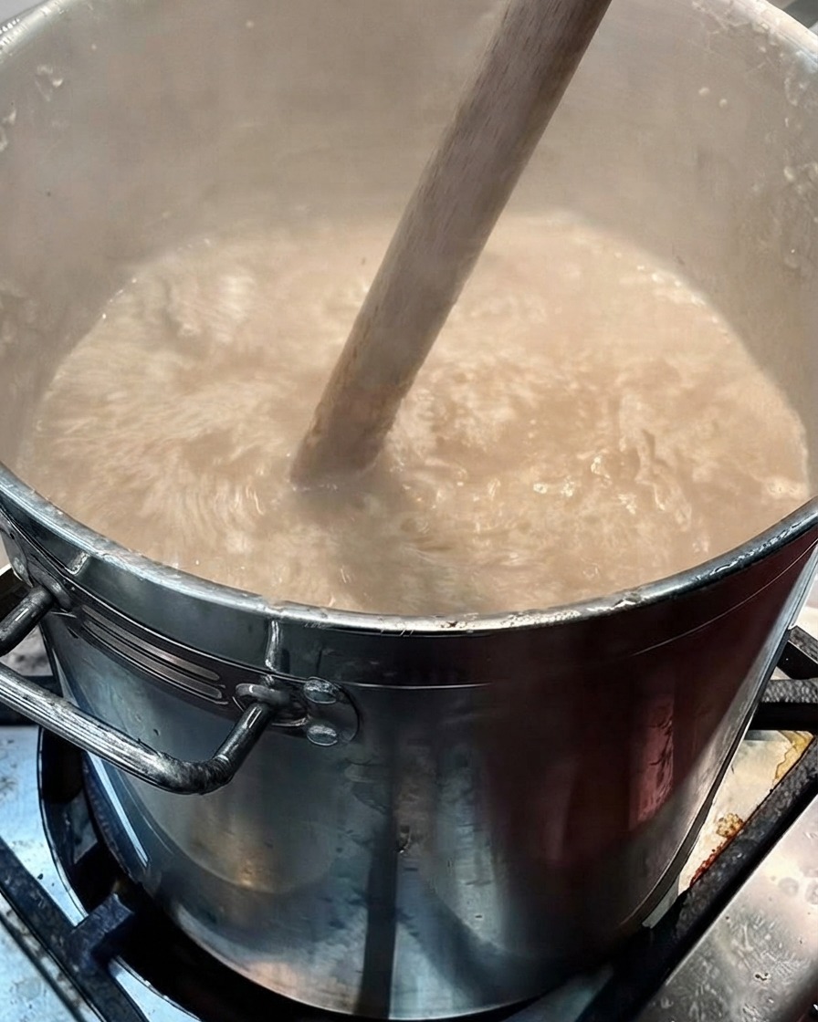 大きな木べらが、薄茶色みがかったスープをかき混ぜている様子。